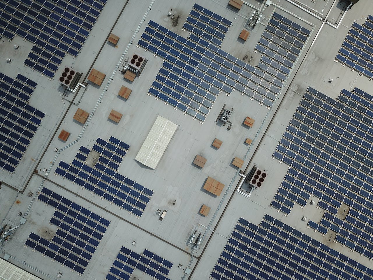about-us High-angle aerial shot of a large rooftop solar panel array on an industrial building.